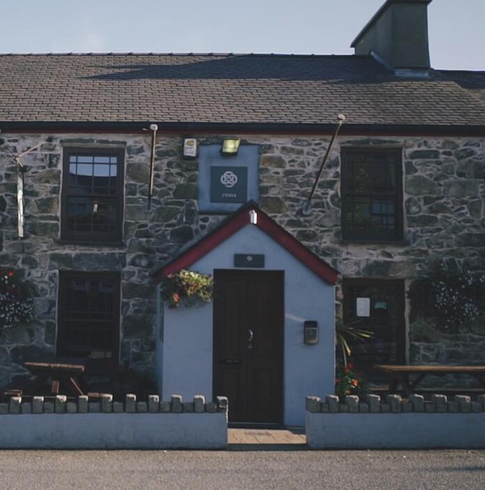 Exterior of a stone built pub with a small garden and benched in front.