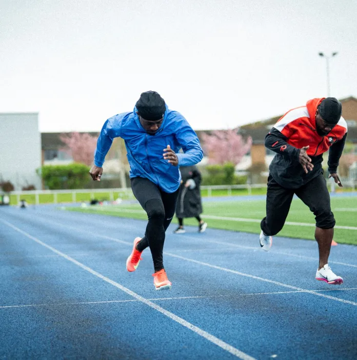 Jeremiah Azu training with fellow sprinters on an outdoor athletics track.