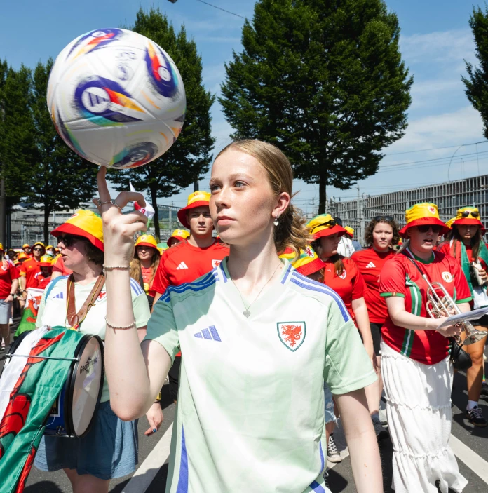 A Wales football fan spins a ball on her finger while supporters and musicians march behind her.