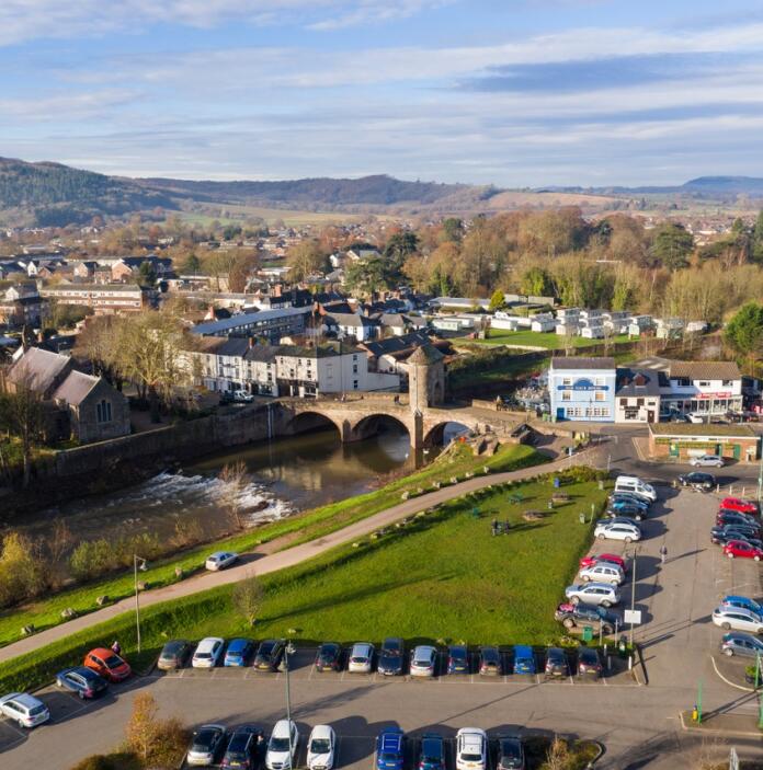Aerial shot of a Welsh market town with a river, green banks and old bridge