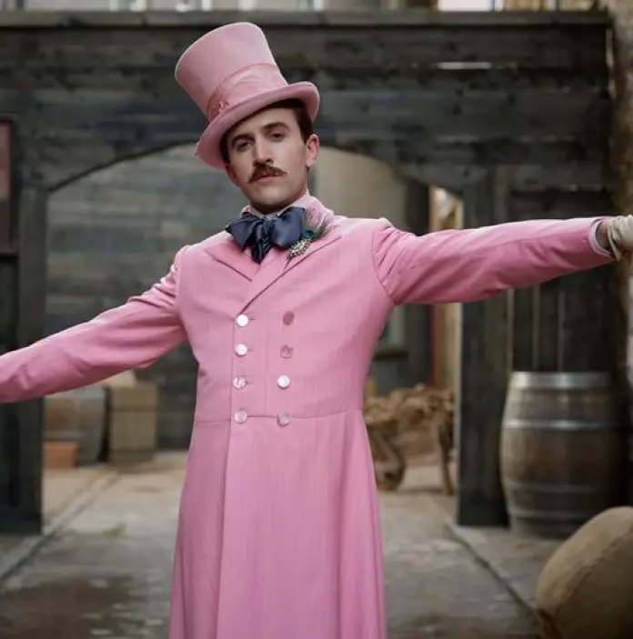 A man in a pink suit and top hat standing with arms out wide.