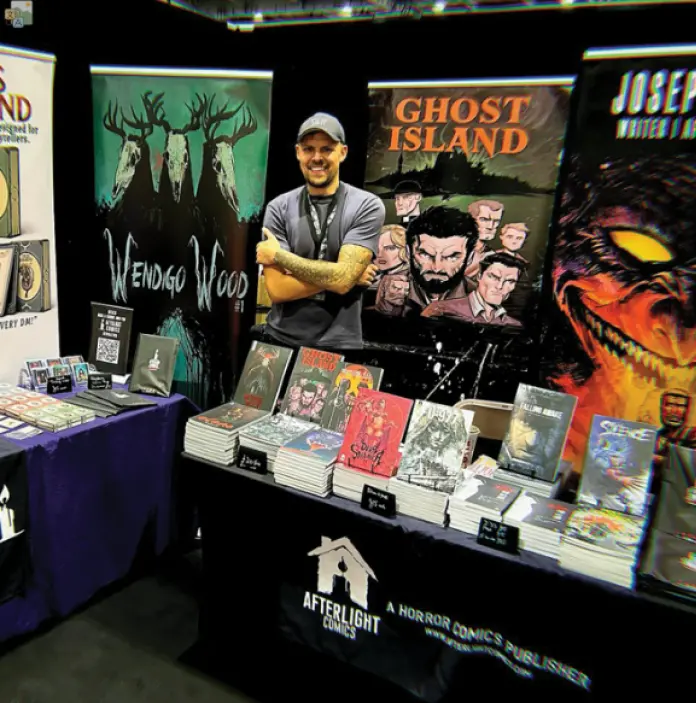 A comic convention stand showcasing horror comics from Afterlight Comics, with the creator standing behind the display. 