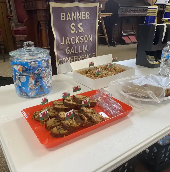 A table is set with snacks, drinks, and refreshments for visitors. A banner and serving items are displayed nearby. 