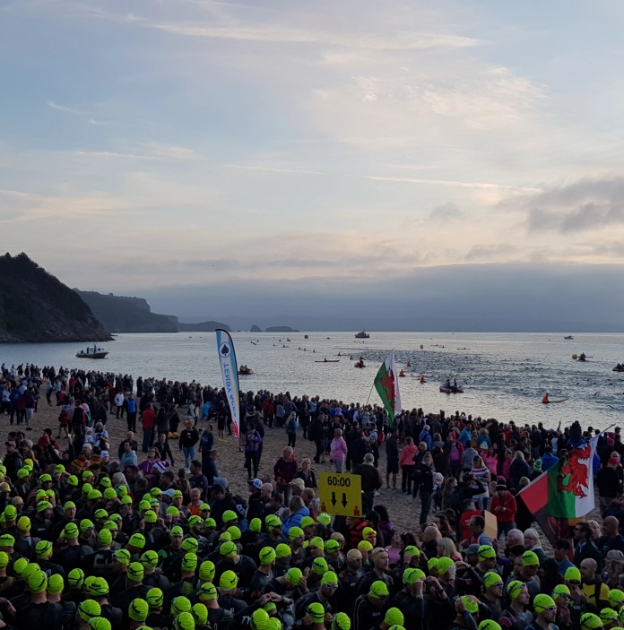 Des centaines de triathlètes rassemblés sur une plage au lever du soleil regardent vers la mer.