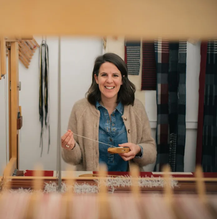 Welsh textile artist Llio James sitting at her hand weaving loom, smiling at the camera