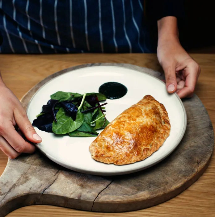 A beautifully presented plate with a Welsh oggie (pasty) and salad, on a wooden board