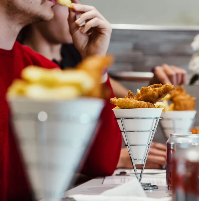Diners enjoying fish and chips served in white cone-shaped containers at a restaurant table. 