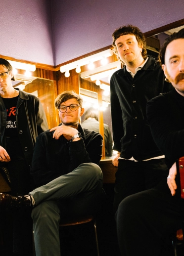 Four men sat in a theatre dressing room.