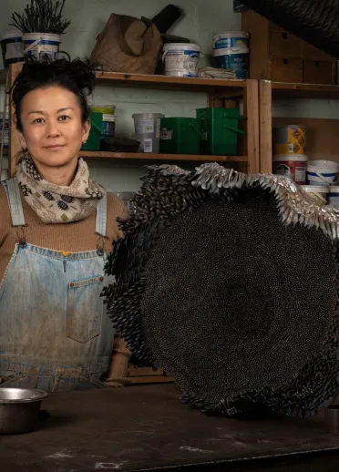 An artist standing in a workshop next to an intricate black sculpture