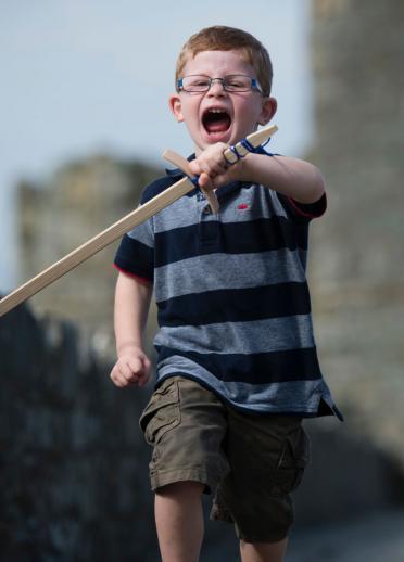 Boy in focus running with play sword through Harlech Castle which is blurred in the background.