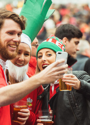 Three Welsh rugby fans taking a selfie in a crowd