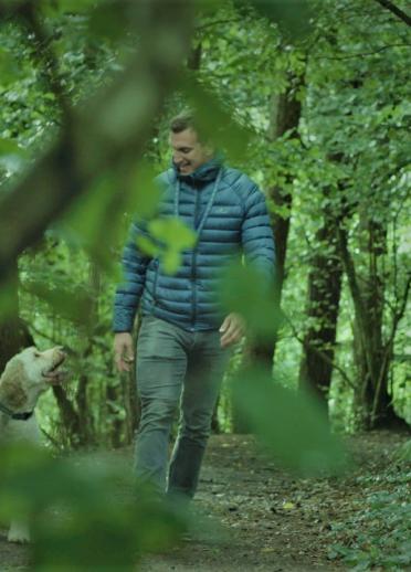 Sam Warburton walking his dog in the woods, seen through the leaves of trees