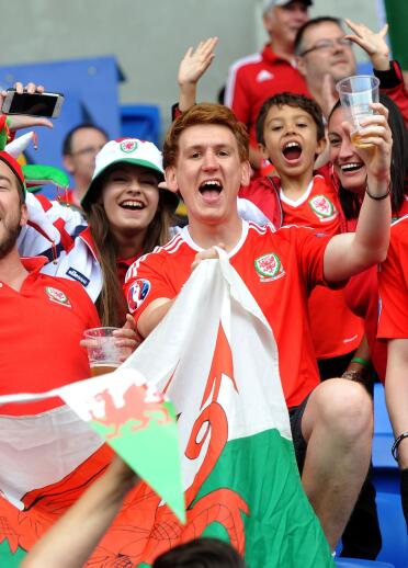 A group of people with Wales football shirts on smiling and holding the Welsh flag.