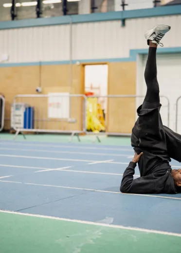 Jeremiah Azu stretching on an indoor athletics track during a training session.
