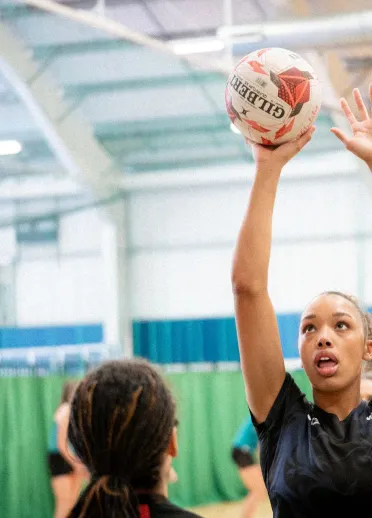 Team Wales netball player shoots during a training drill as a teammate contests the ball on an indoor court.