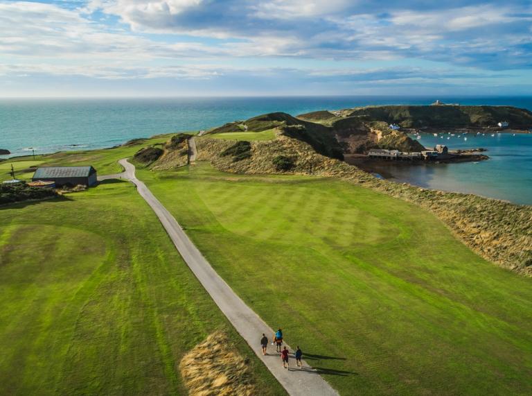 An aerial shot of a path leading to a headland surrounded by the sea 