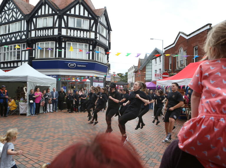 People dancing in the centre of the town with a crowd watching.