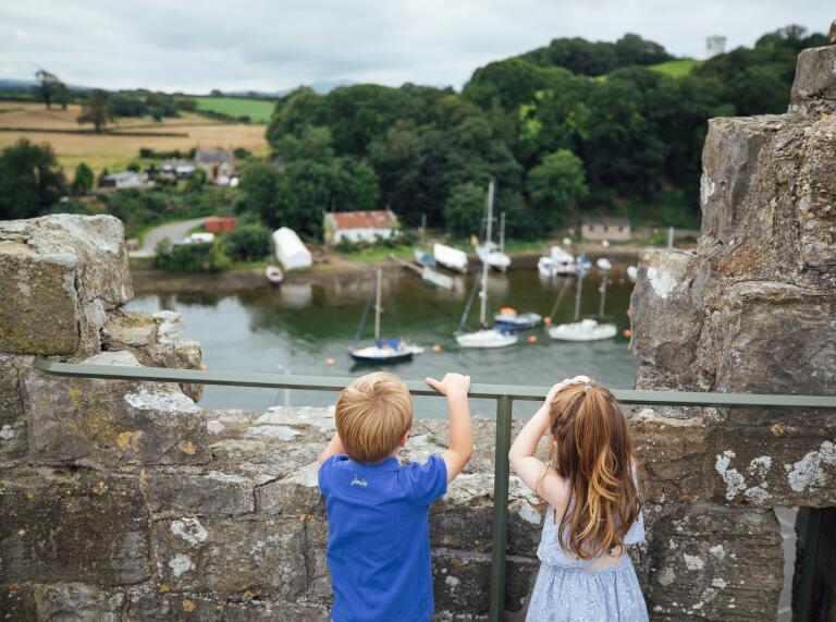 A little boy and a girl looking out over the castle walls at the boats.