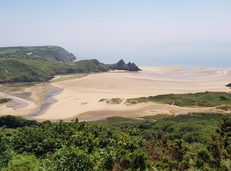 A sandy beach surrounded by green landscape and the sea.