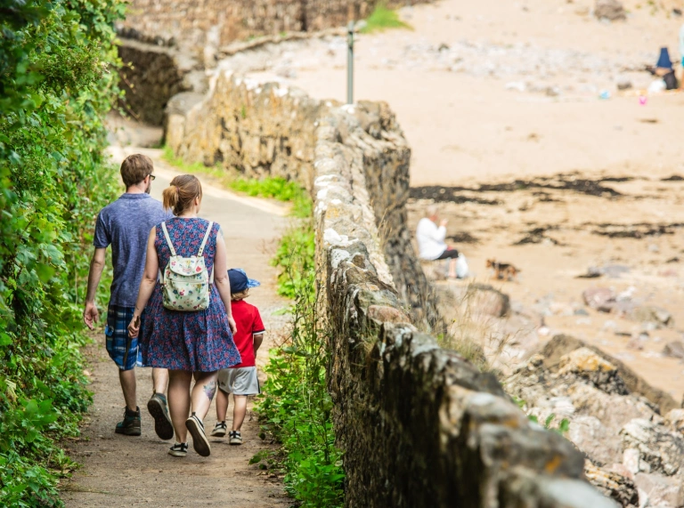 A family walking down a path to the sandy beach.