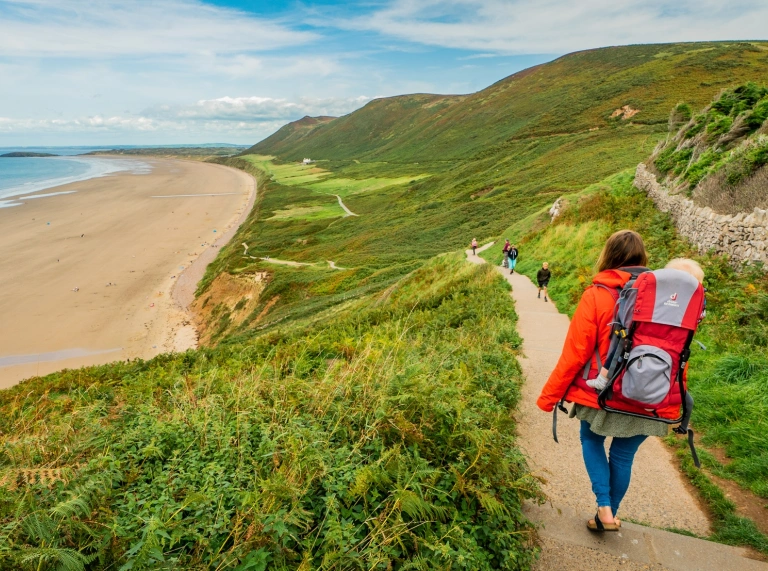 A hiker walking down a steep path to the beach.
