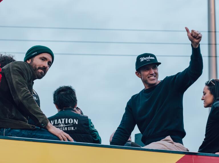 The two managers of the team waving from the bus.