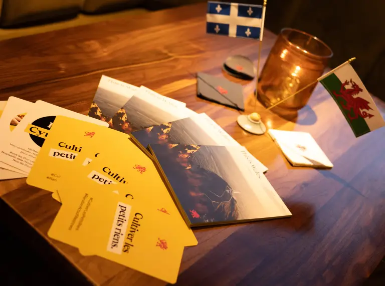 Welsh and Québec table flags beside Cymru Wales brochures and cards on a wooden table.