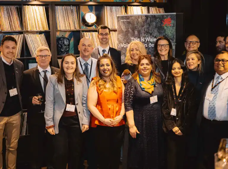 Group of event attendees posing in front of a “This is Wales” display and shelves of vinyl records.