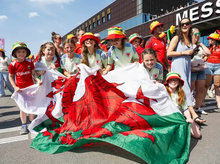 Young Cymru supporters hold a large Welsh flag as they gather with fellow fans ahead of a UEFA Women's EURO 2025 match in Switzerland. 