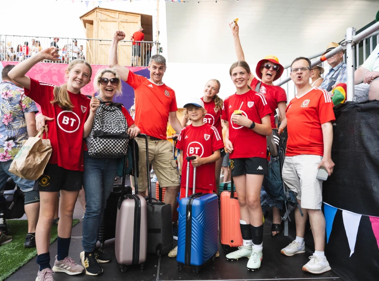A group of Cymru supporters wearing red Wales shirts pose with their luggage after arriving in Switzerland for UEFA Women's EURO 2025 