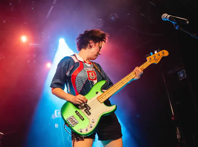 A member of Adwaith plays bass guitar on stage during a performance for Cymru supporters at UEFA Women's EURO 2025 