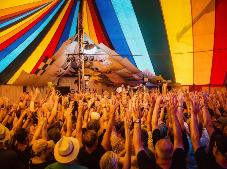 A tent full of people with their hands in the air and musicians playing on a stage.