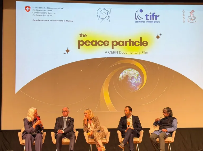 Five panellists seated on stage during a discussion at a screening of The Peace Particle, a CERN documentary film, with the film’s title displayed on a large screen behind them.