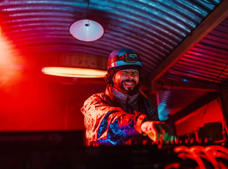 DJ Roni Size wearing a helmet and headtorch while performing beneath red and blue lights at Cwmorthin Slate Mine. 