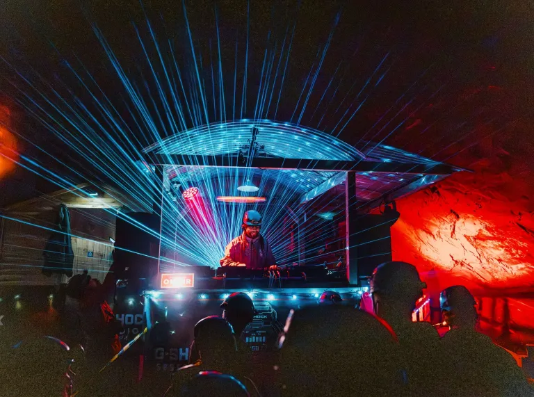 DJ Roni Size performing beneath blue laser lights as helmeted revellers dance inside Cwmorthin Slate Mine. 