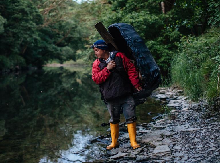 Un homme portant un coracle, debout sur les berges de la rivière