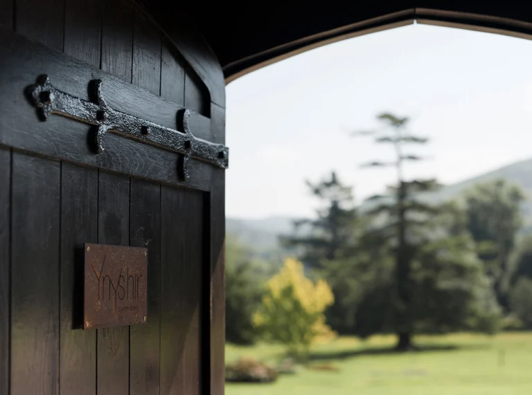 porte en bois ouverte en avant plan, avec des arbres et de l'herbe flous en arrière-plan