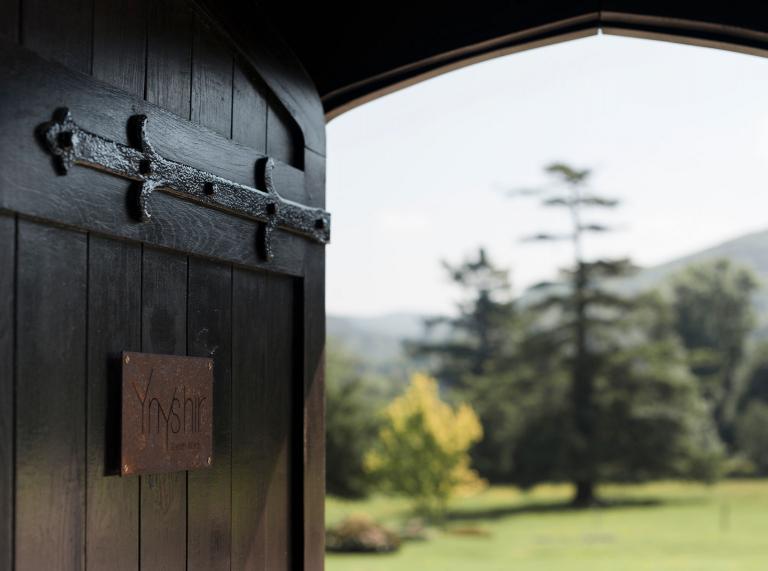 open wooden door in focus, with blurred trees and grass in background