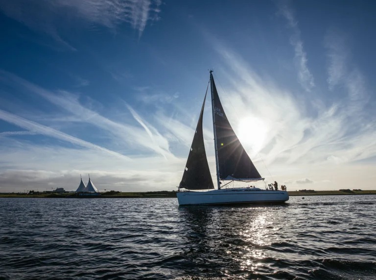 Silhouette eines Bootes, das an einem klaren Tag entlang der Cardiff Barrage fährt und die Sonne verdeckt.