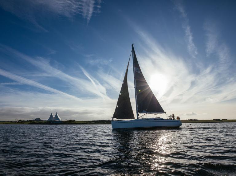 Un bateau, en silhouette, navigue le long du Barrage par temps clair, bloquant le soleil.