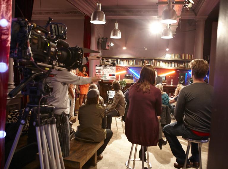 filming of actors taking place in a television studio on a drama set