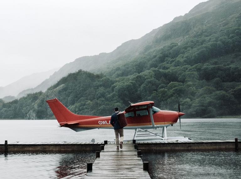 Luke Evans walking down pontoon over a lake towards a small aircraft