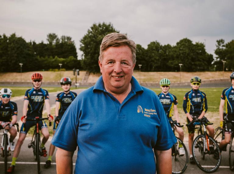 L'entraîneur de cyclisme Alan Davies MBE au premier plan avec des membres du Maindy Flyers Youth Cycling Club debout avec des vélos derrière.