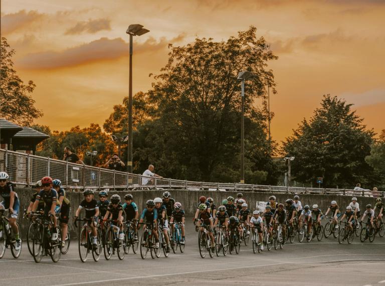 Ciclistas en una pista de ciclismo al aire libre con puesta de sol en el cielo