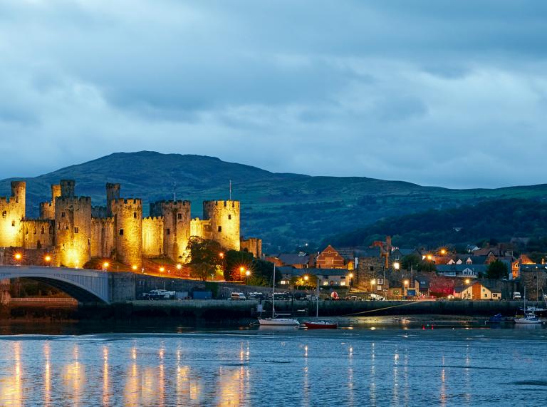 Castillo de Conwy al anochecer iluminado con un reflejo en el agua