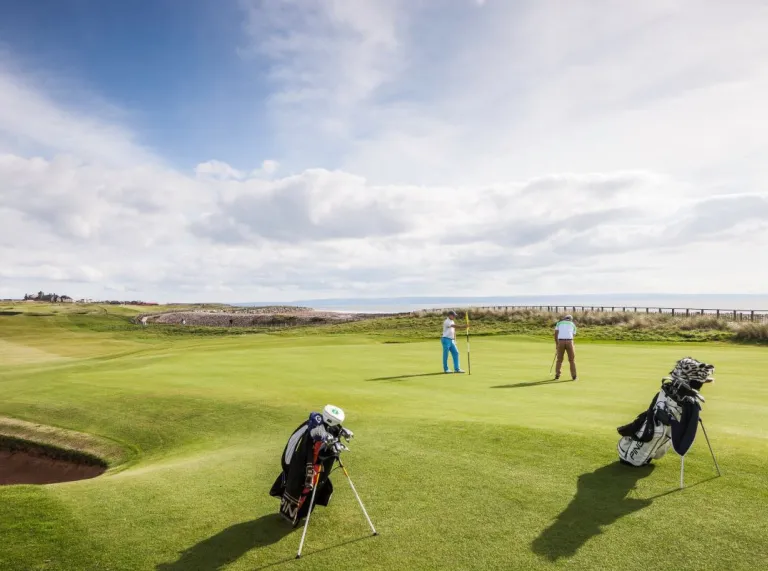 Una escena al aire libre de un hombre jugando al golf contra un cielo azul con el mar de fondo