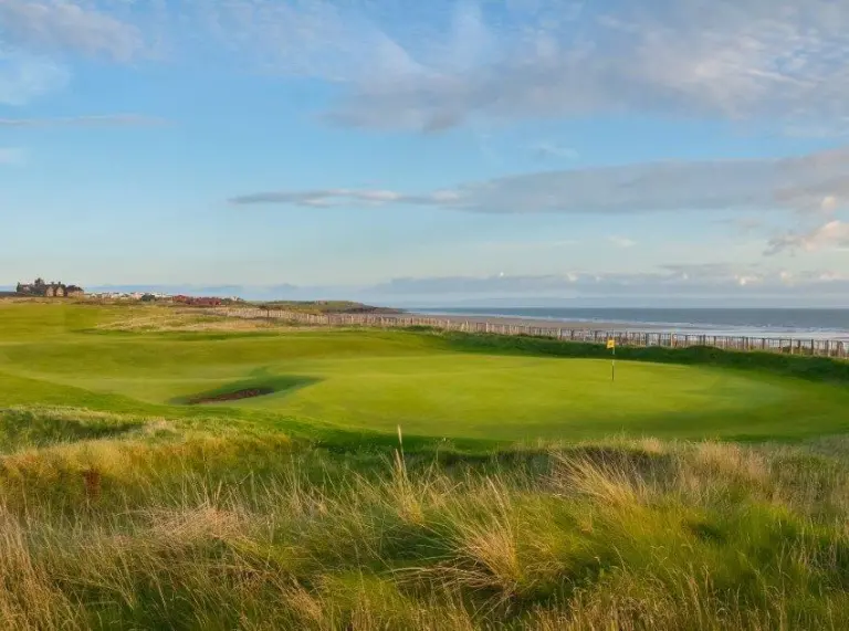 Una escena al aire libre de un campo de golf contra un cielo azul con el mar de fondo