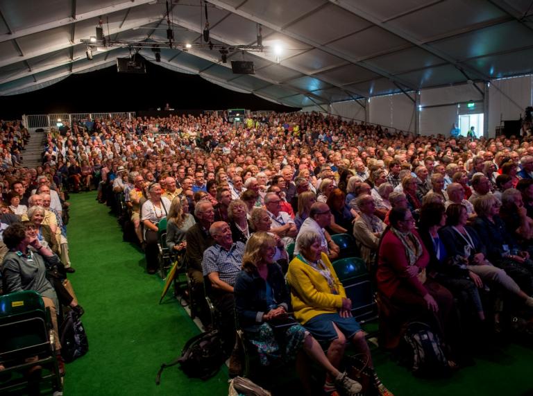 A tent filled with people sitting on chairs looking at a speaker