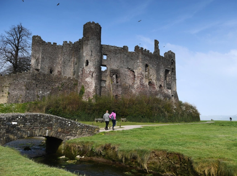 A couple of people walk past a large old ruined castle