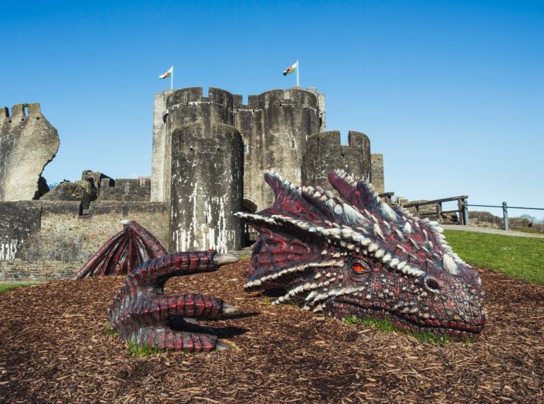A large sculpture of a red dragon in front of a large old castle